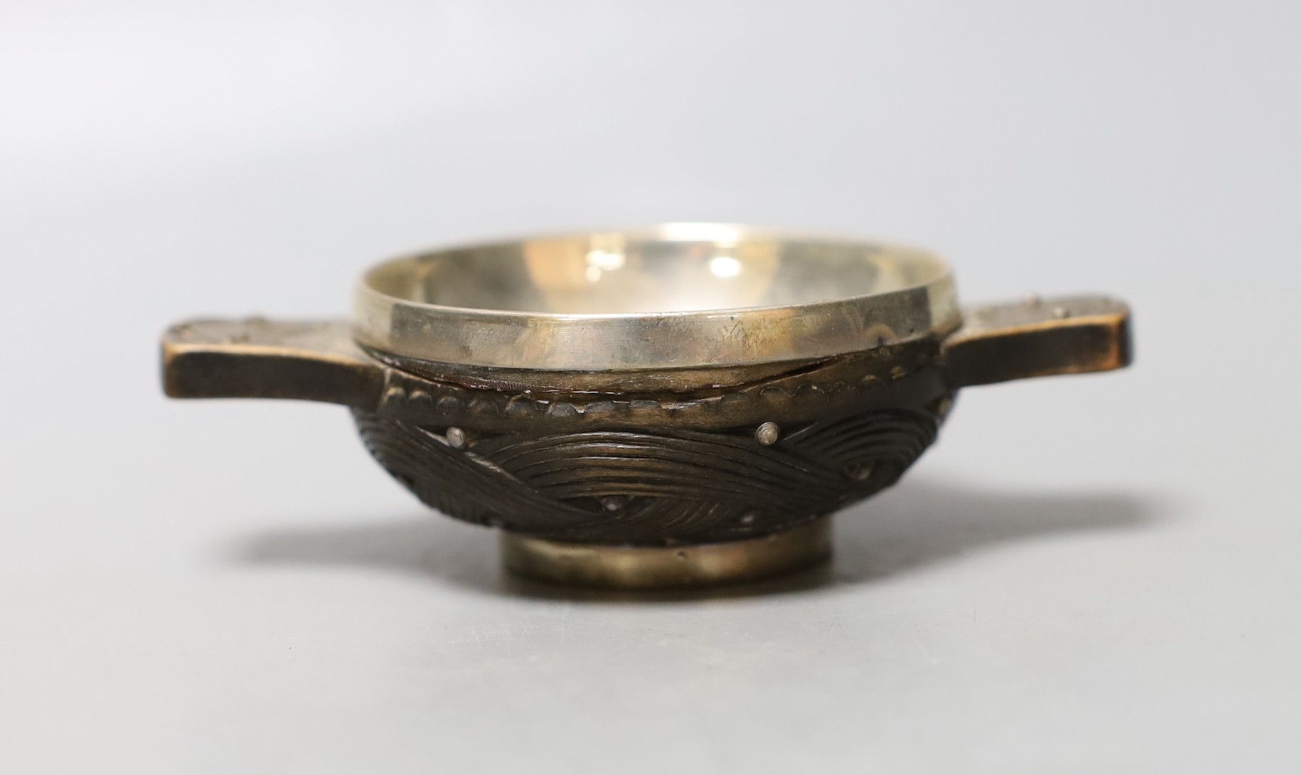 A late 18th/early 19th century white metal mounted wooded quaich, with interwoven carving, unmarked, diameter 11.1cm, (a.f).